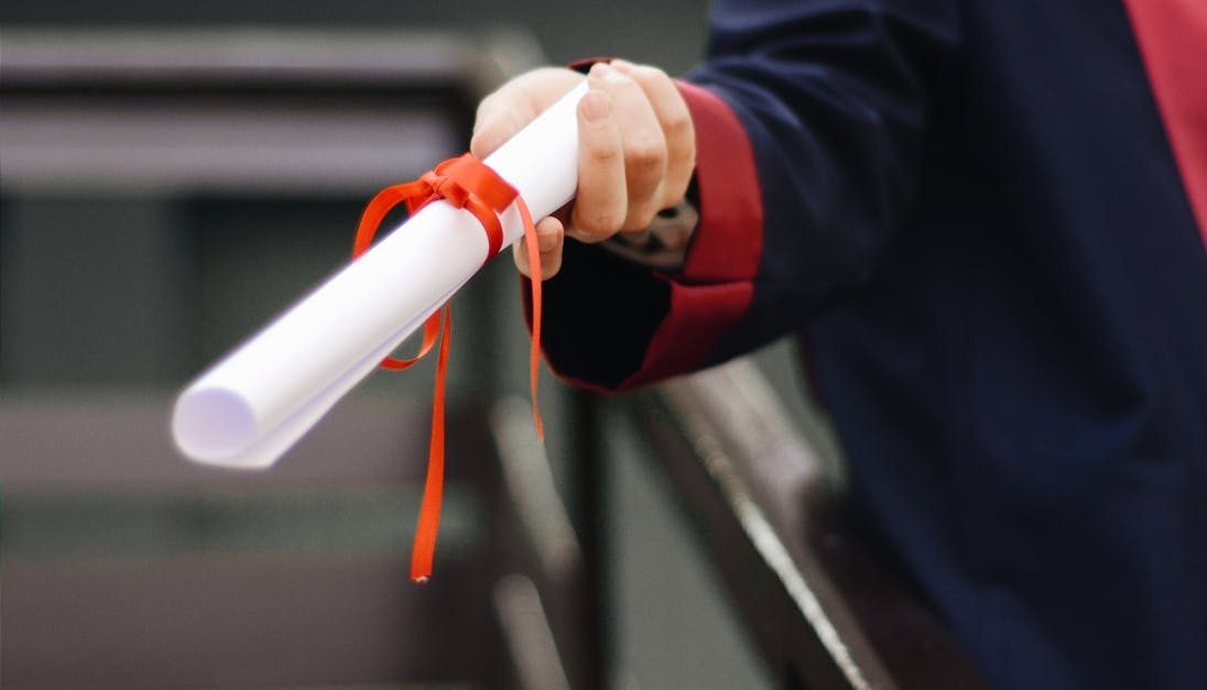 A close-up image of a graduate holding a diploma tied with a red ribbon, symbolizing achievement and success.